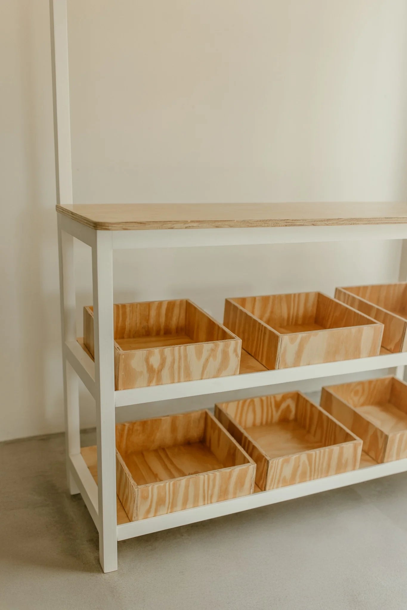 Angled view of kids play shop showing sturdy frame and two-tier shelves with removable wooden bins.