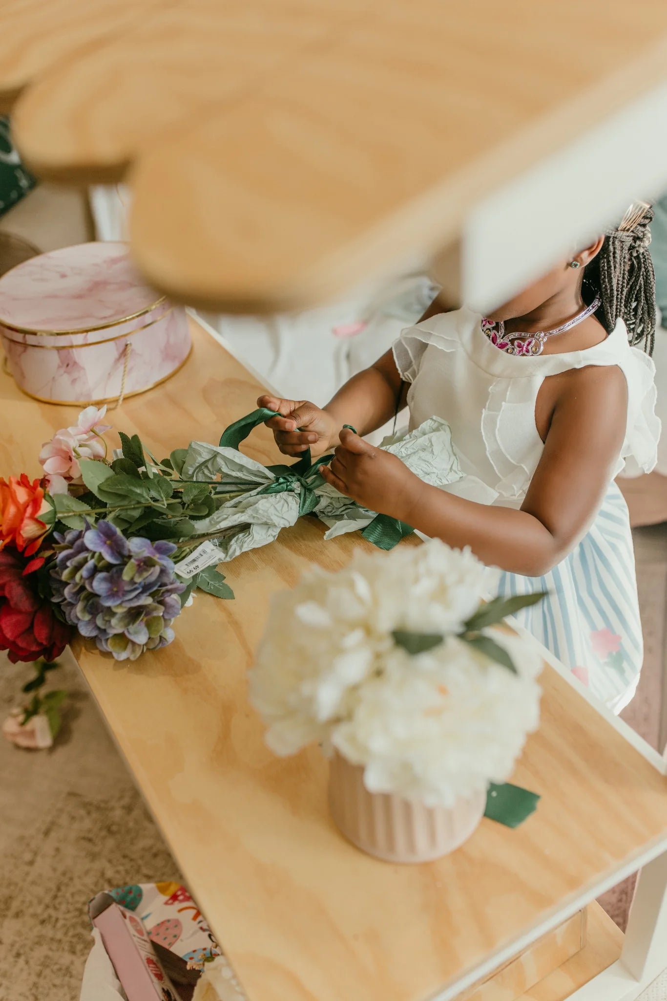 Child’s hands tying ribbon on flowers at the wooden kids play shop counter.