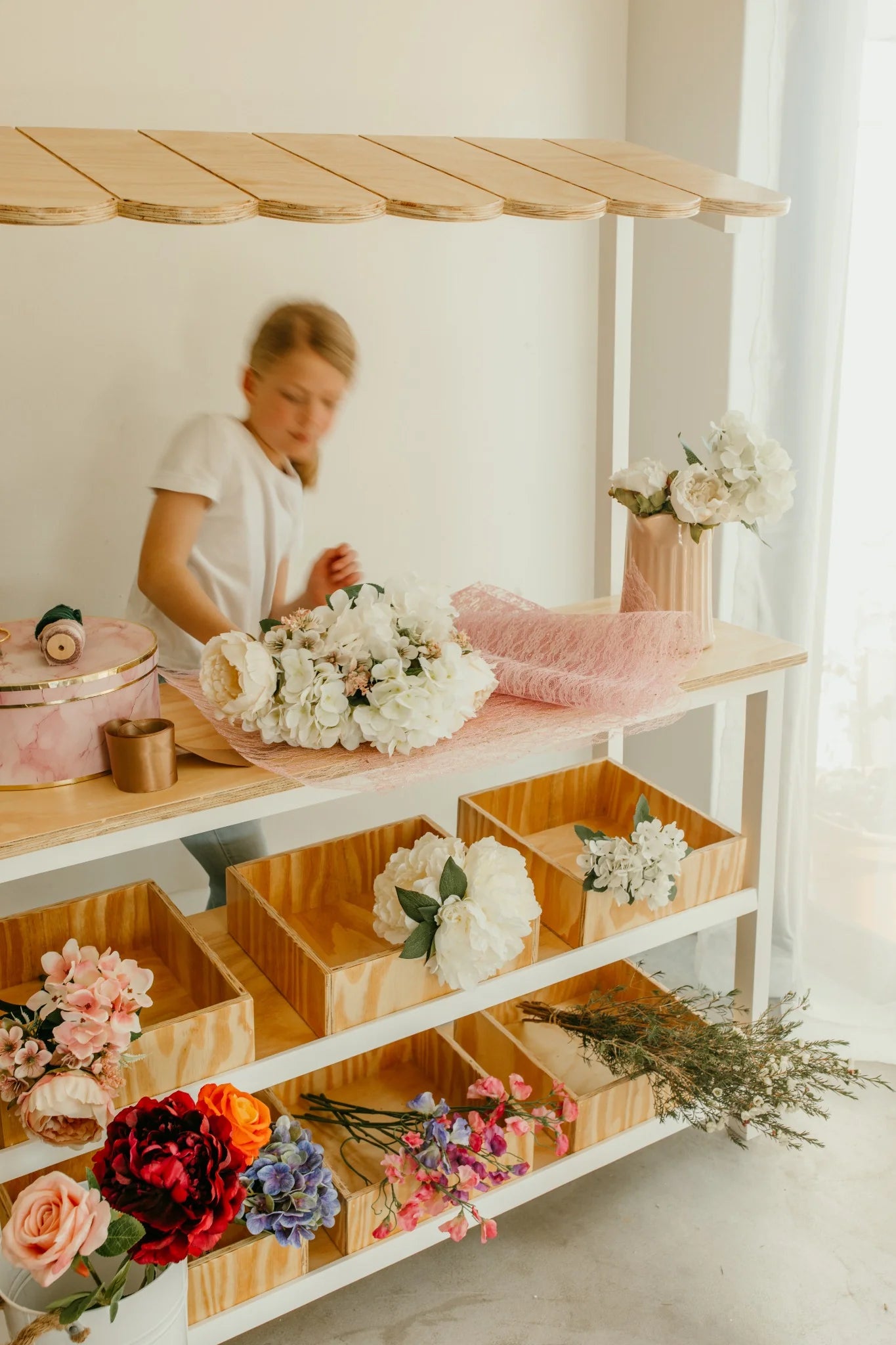 Child playing behind the wooden kids play shop, arranging flowers at the counter.