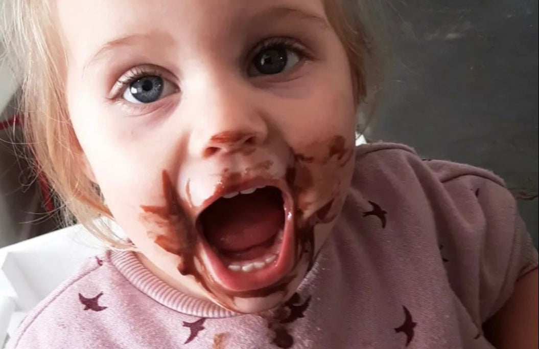 Girl with chocolate covered face helping her mom baking in the kitchen on her Learning Tower