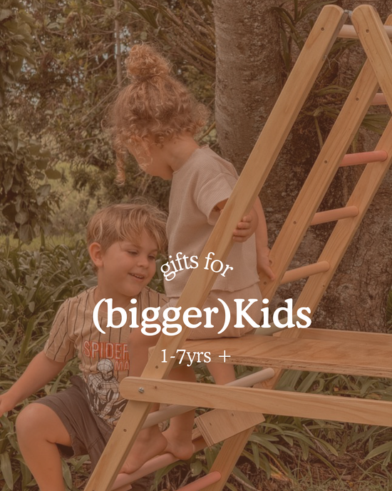 Two young children playing on an outdoor wooden climbing frame under a tree. Text on image reads ‘Gifts for (bigger) Kids, 1–7 yrs +