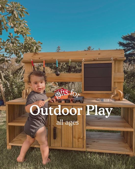 Baby playing at a wooden outdoor mud kitchen in a sunny garden. Text on image reads ‘Gifts for Outdoor Play, all ages