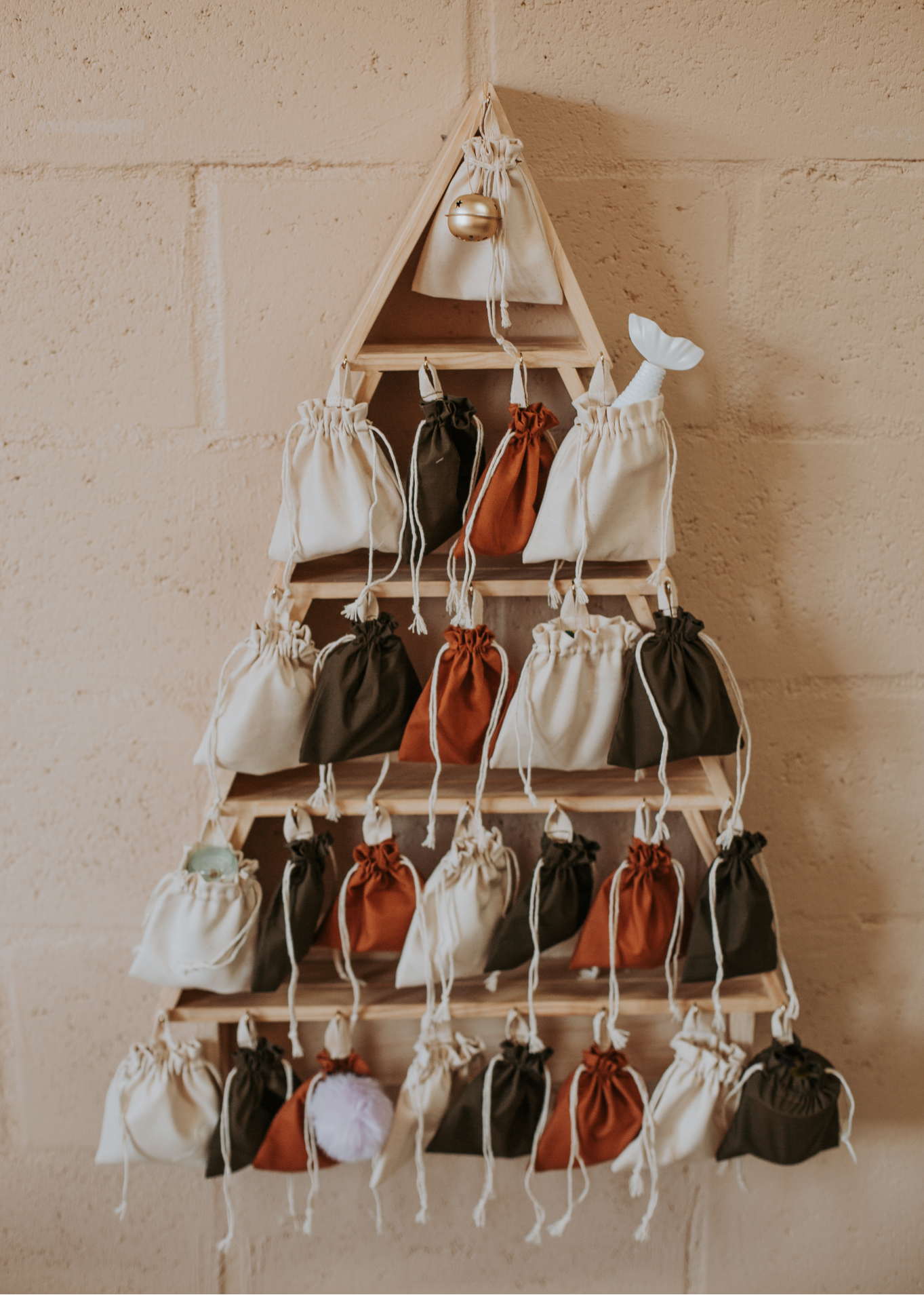 Wooden Christmas tree-shaped advent calendar filled with small fabric drawstring bags in earthy colours