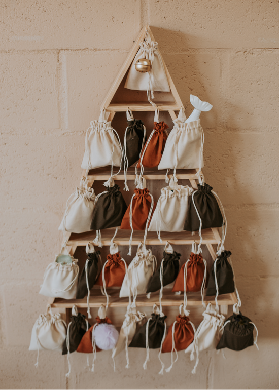 Wooden Christmas tree-shaped advent calendar filled with small fabric drawstring bags in earthy colours