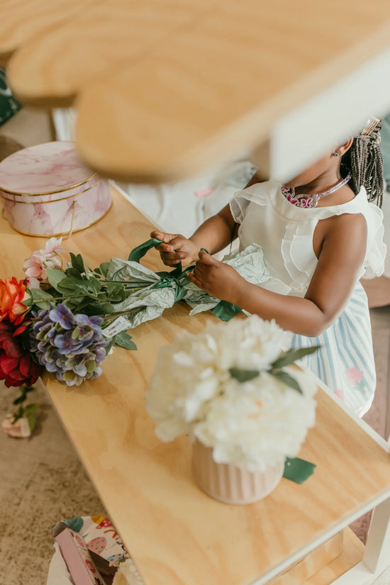 Child’s hands tying ribbon on flowers at the wooden kids play shop counter.