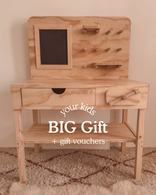 Wooden kids’ workbench with pegboard, drawer and shelves, photographed in a warm, cosy playroom. Text on image reads ‘Your Kids BIG Gift + gift vouchers.