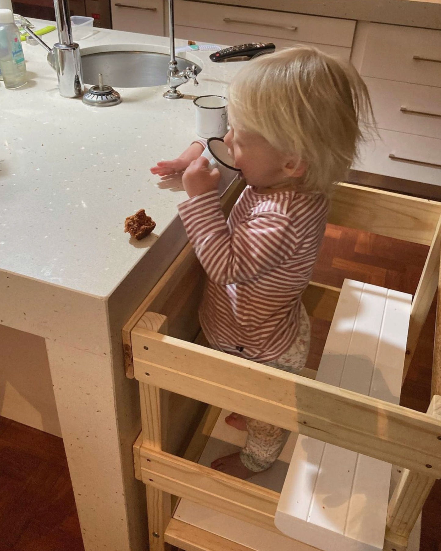 Toddler enjoying a snack while seated on the wooden Learning Tower seat add-on