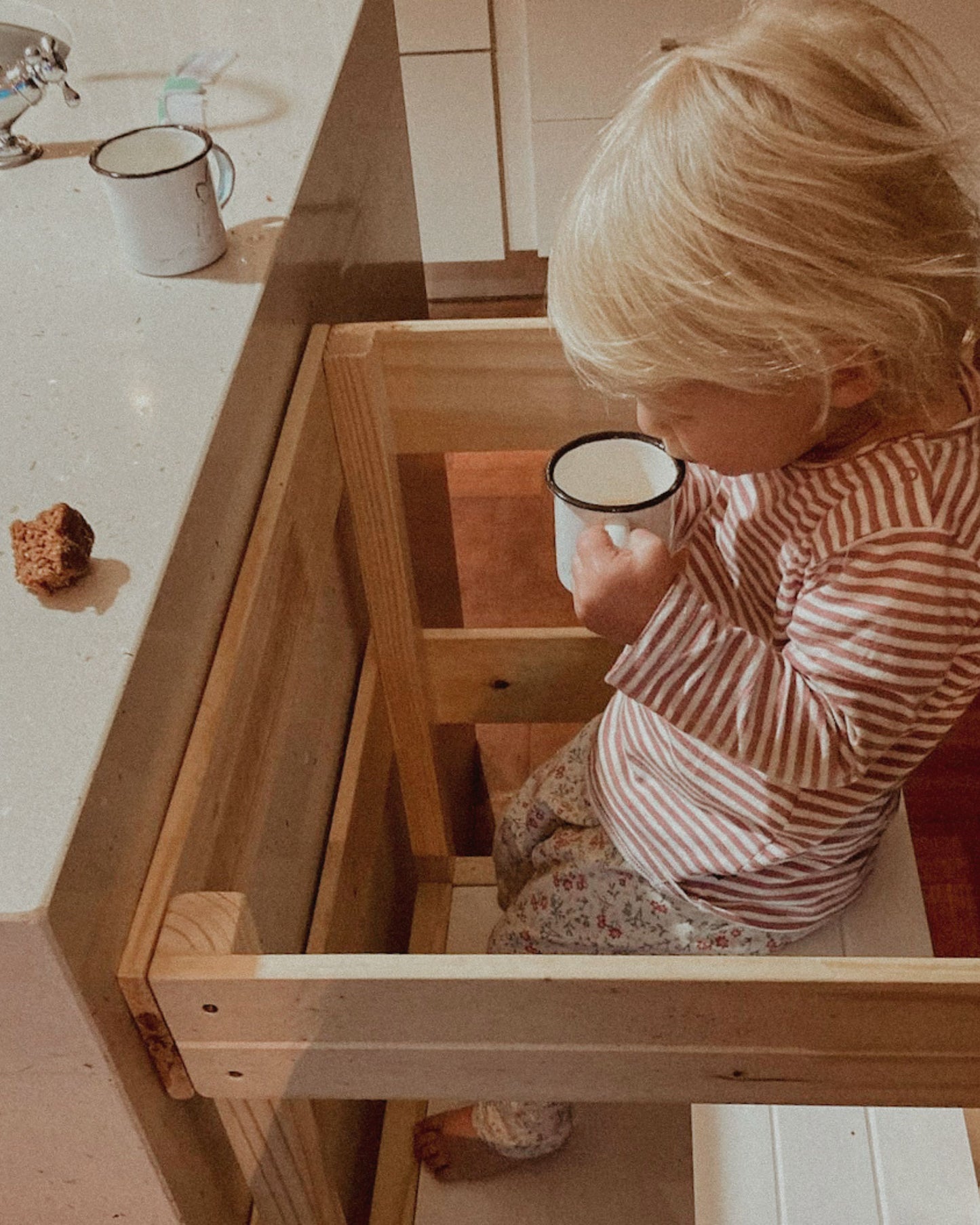 Toddler sitting securely on the Learning Tower seat add-on while drinking at the counter.