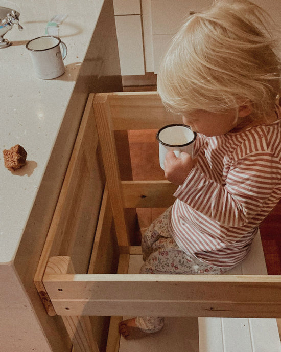 Toddler sitting securely on the Learning Tower seat add-on while drinking at the counter.