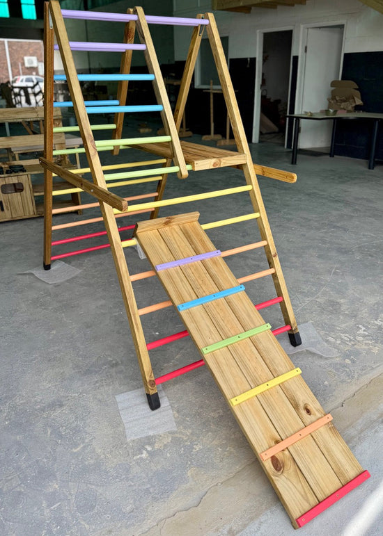 Outdoor Pikler Playground in an expanded setup, featuring rainbow-coloured climbing rungs and a wooden slide, handcrafted from treated timber for outdoor use.