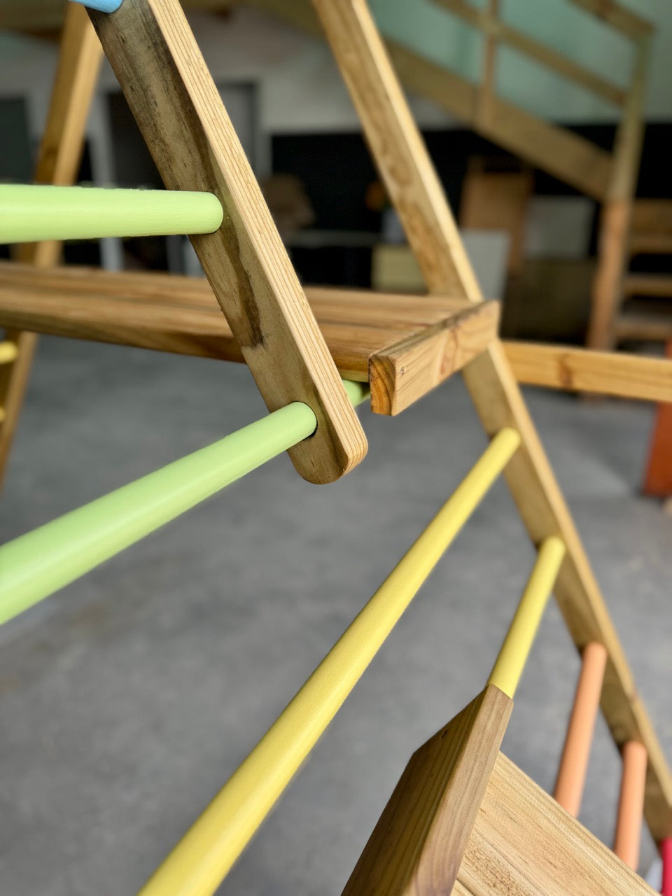 Close-up of the small wooden platform and reversible ramp on the Outdoor Pikler Playground, showing how the ramp hooks securely over the climbing rungs for safe, stable play