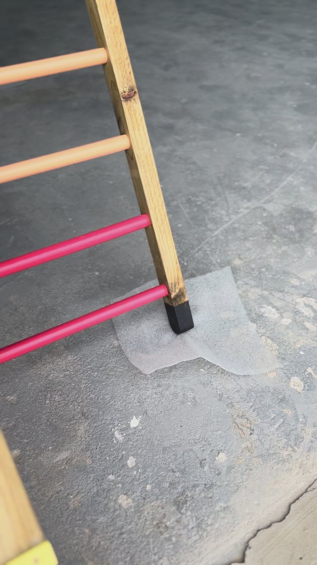 Load and play video in Gallery viewer, Video panning upward from the bitumen-sealed feet of the Outdoor Pikler Playground to the reversible ramp with the ramp side facing up, showing the treated timber frame and rainbow-coloured climbing rungs.
