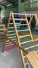 Video starting with a tight side view of the Outdoor Pikler Playground, then stepping back to reveal the full reversible ramp in slide mode, with rainbow-coloured climbing rungs and a treated-timber frame.