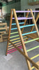 Side-profile video of the Outdoor Pikler Playground showing the ramp side of the reversible ramp facing upward, with pastel rainbow climbing rungs on the treated-timber frame.