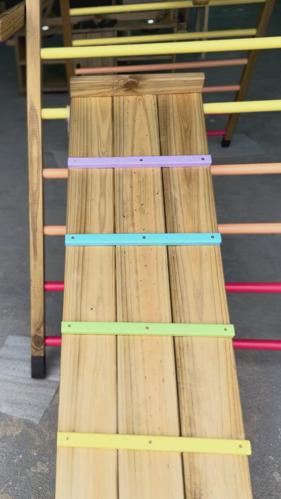 Load and play video in Gallery viewer, Close-up video panning over the Outdoor Pikler Playground ramp, showing the treated timber surface and pastel climbing rungs designed for outdoor use
