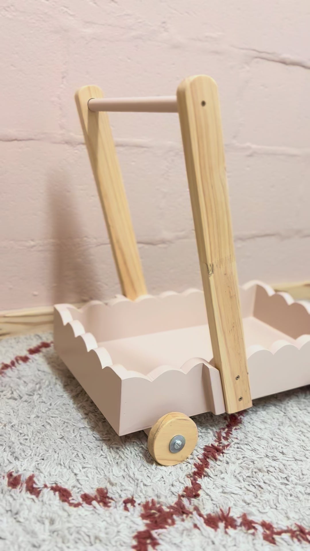 Load and play video in Gallery viewer, Scalloped wooden baby push walker in blush linen finish shown from side angle indoors.
