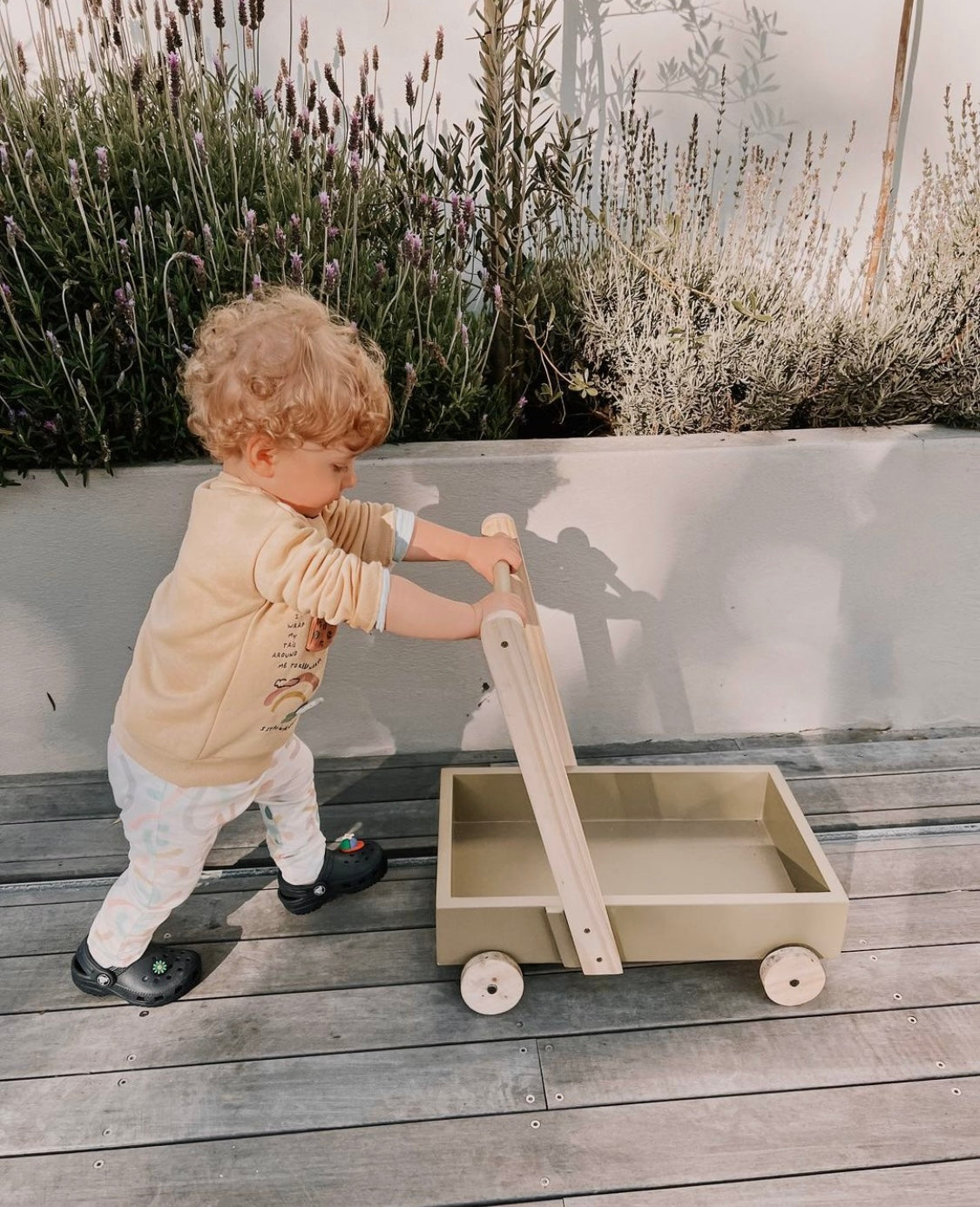 Toddler taking first steps while pushing a wooden baby walker on a deck outdoors, handcrafted push walker by Grandpa’s Workshop