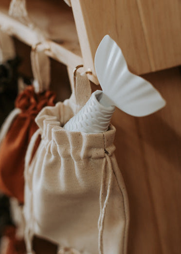 Close-up of a fabric drawstring bag on a wooden advent calendar, with a small white mermaid-tail toy peeking out