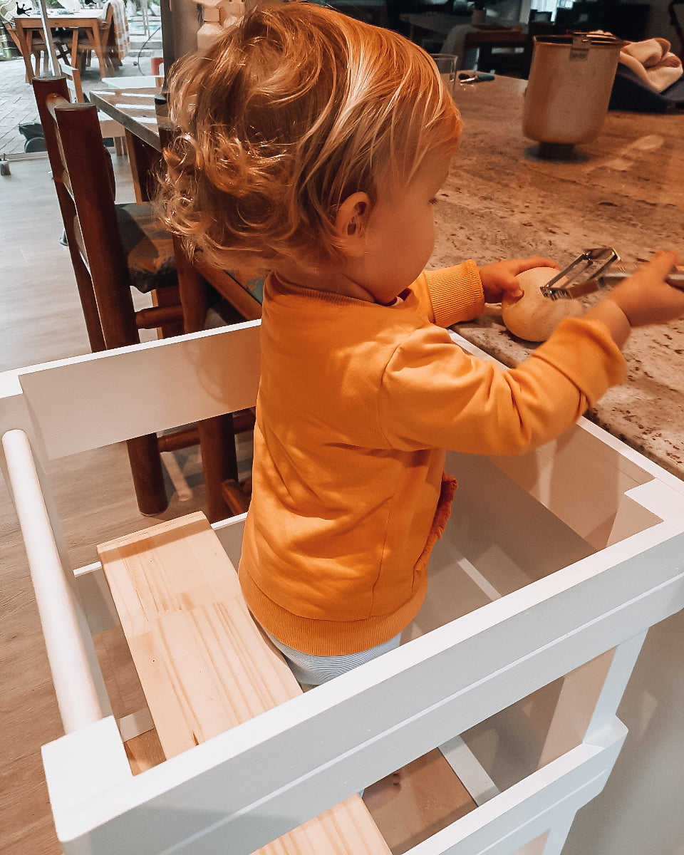 Toddler in orange top playing while seated on the Learning Tower seat add-on