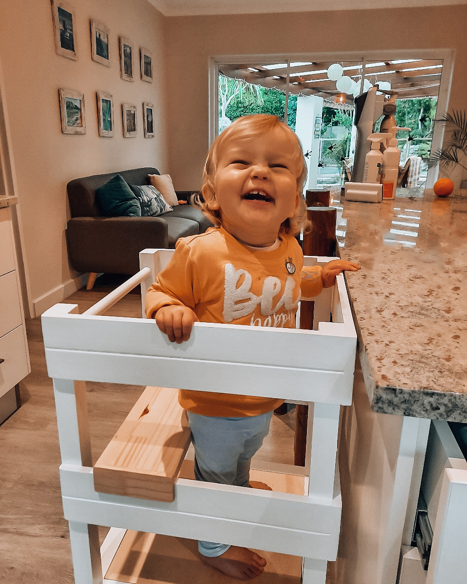 Happy toddler seated in a Learning Tower with seat add-on, white finish