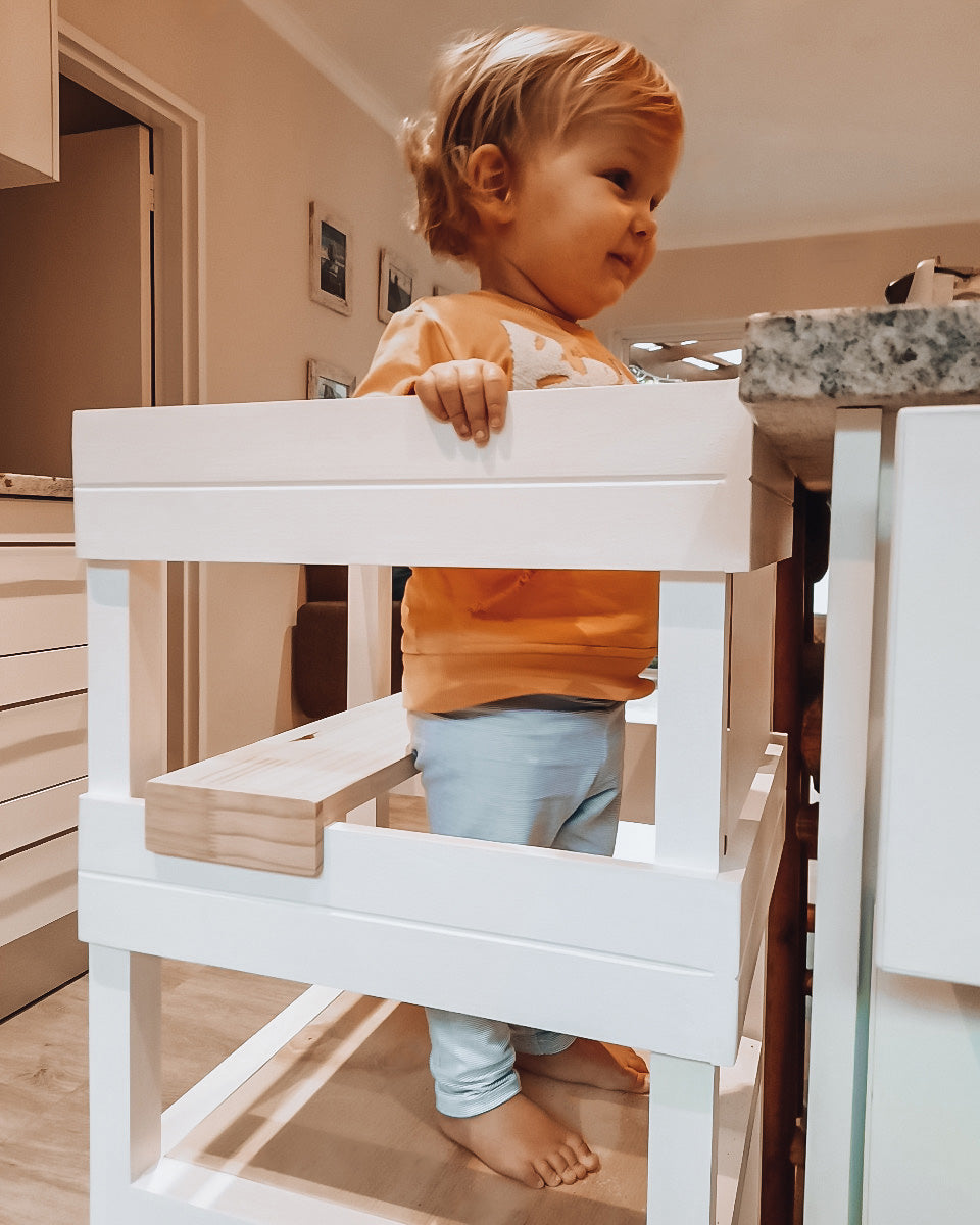 Toddler smiling while seated in a white Learning Tower with seat add-on